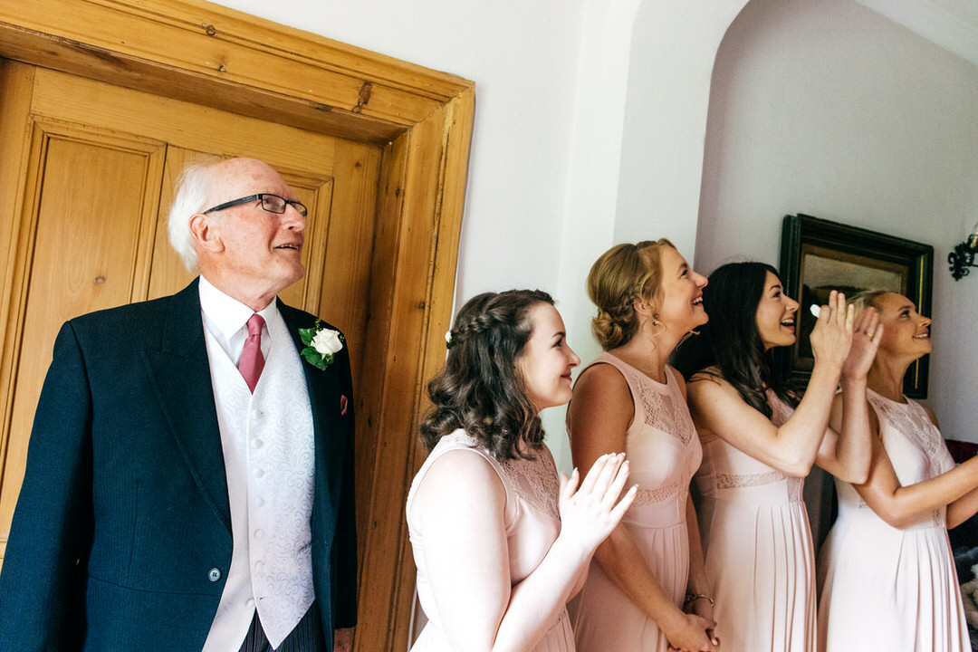 Brides dad and bridal party wait for the bride to come down stairs and reveal her outfit 